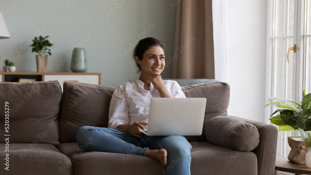 Happy pretty Indian laptop user girl working at laptop from home, thinking over online project, success, achieve, touching chin, looking at window away, smiling, resting on couch, enjoying leisure Happy pretty Indian laptop user girl working at laptop from home, thinking over online project, success, achieve, touching chin, looking at window away, smiling, resting on couch, enjoying leisure