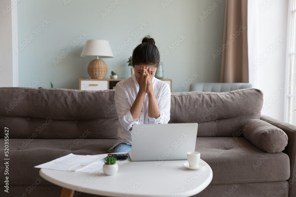 Frustrated young woman touching face with closed eyes over heap of paper bills, documents, calculator, sitting on couch at laptop computer, thinking over overspending, bankruptcy Frustrated young woman touching face with closed eyes over heap of paper bills, documents, calculator, sitting on couch at laptop computer, thinking over overspending, bankruptcy