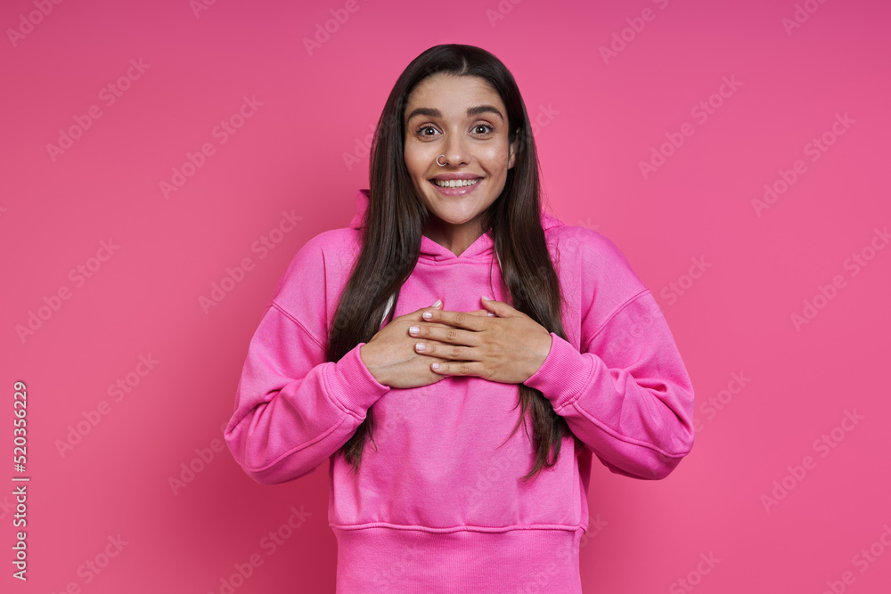 Surprised young woman in hooded shirt looking at camera and smiling against pink background Surprised young woman in hooded shirt looking at camera and smiling against pink background