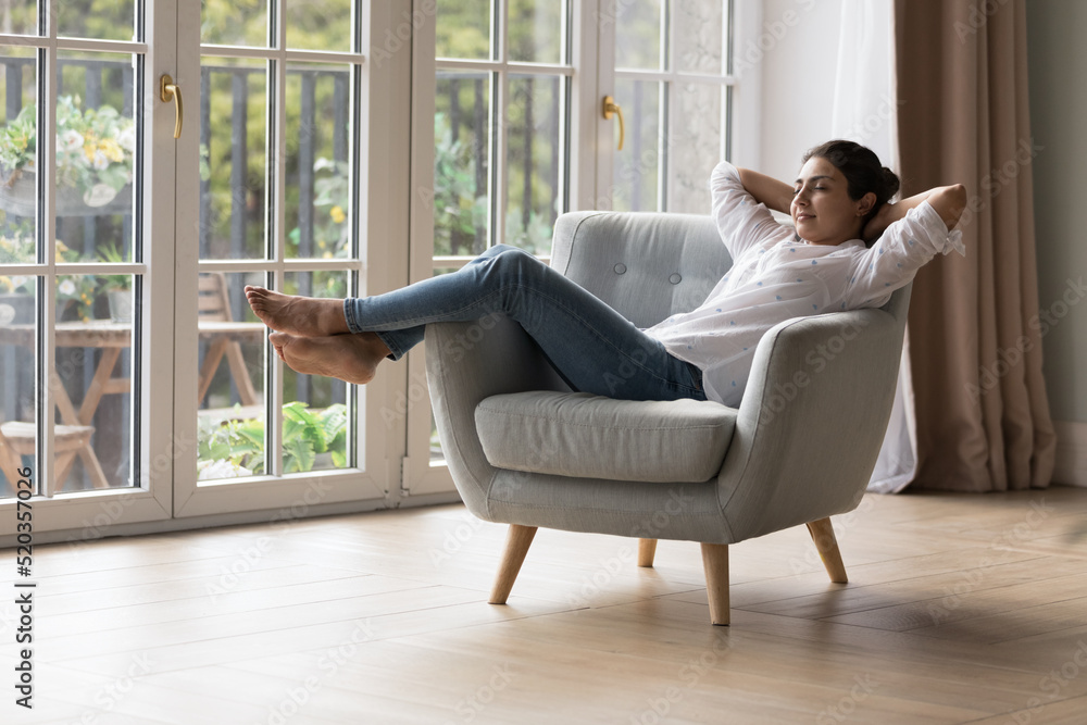 Calm peaceful lazy young Indian homeowner woman resting in armchair with closed eyes at big terrace window, breathing fresh cool air, enjoying peace, leisure, comfort, meditating at home Calm peaceful lazy young Indian homeowner woman resting in armchair with closed eyes at big terrace window, breathing fresh cool air, enjoying peace, leisure, comfort, meditating at home