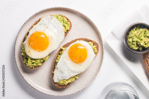 Avocado egg sandwich with a glass of water. Healthy light breakfast concept. Whole grain toasts with mashed avocado and fried eggs