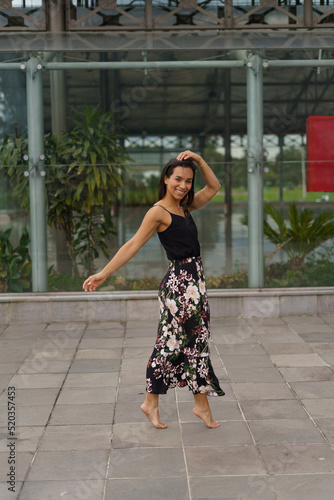 dancing on tiptoes a young latin woman wears a summer dress with a printed skirt has short hair, city lifestyle, hobbies