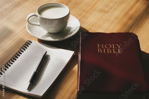 Pray and study the Bible in the morning in the warm sunshine on a bright day.  with a cup of coffee and a notebook  Placed on a wooden table under the bright morning sun.