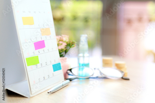 Close up business desk calendar with paper notes and office equipment concept of event planner or personal organization reminder and schedule or planning.
