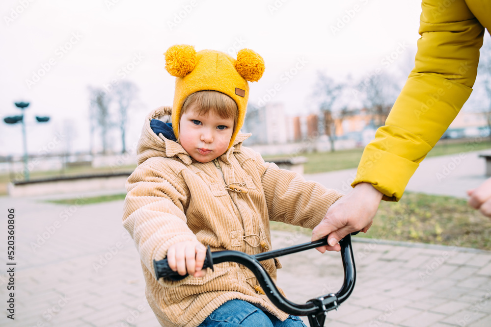 Grandmother teaches small child to ride bike for the first time in city spring Grandmother teaches small child to ride bike for the first time in city spring