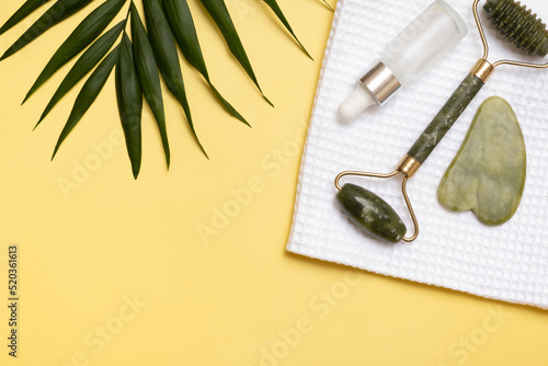 jade stone face roller massager and cosmetic oil and for beauty facial massage therapy with towel. Flat lay on yellow background