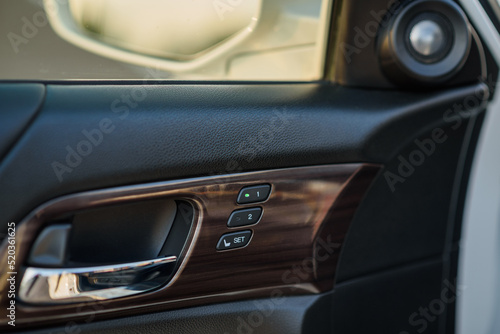Car inside door chrome handle. Door trim. Black and brown new car interior. Clean door leather and panel. Left Panel with seat settings drivers. Buttons to adjust the driver's seat memory. Closeup. © Serhii