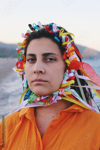 Art portrait of young woman looking at camera with a crown of ribbons on her head