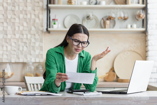 Beautiful woman in a green shirt in despair, received a letter of bad news, brunette reads a message with sadness in the kitchen at home photo