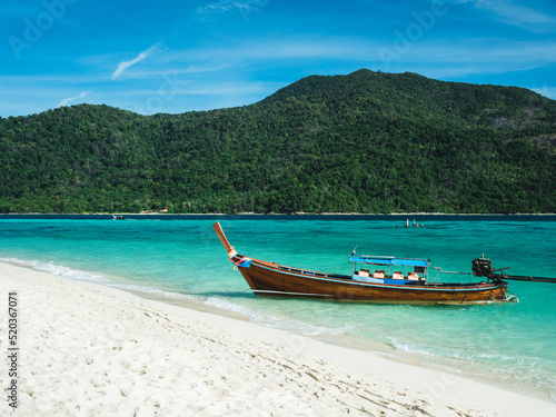Scenic view of local long tail boat at Sunrise Beach, Koh Lipe Island. Tropical white sand beach with crystal clear turquoise sea water against summer blue sky. Satun, Thailand.