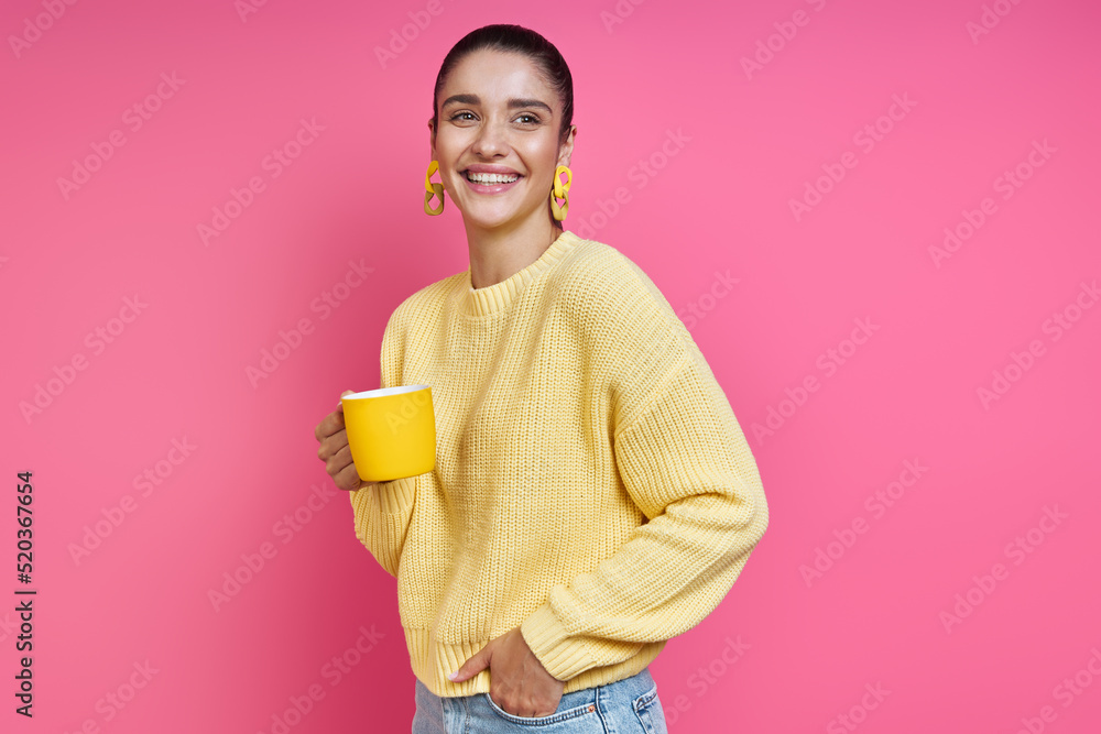 Beautiful young woman in yellow sweater holding coffee cup and smiling against colored background Beautiful young woman in yellow sweater holding coffee cup and smiling against colored background