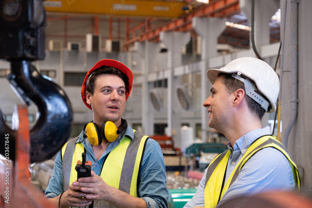 Selective focus at Caucasian men mechanical engineer, wearing safety equipment. While doing machine maintenance and safety control inside of factory area. With blurred background of heavy machine. Selective focus at Caucasian men mechanical engineer, wearing safety equipment. While doing machine maintenance and safety control inside of factory area. With blurred background of heavy machine.