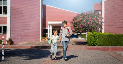 Children with backpacks happily going out from the school after lesson classes. Running in the school yard. Panoramic banner, copy space for text.