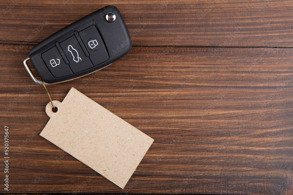 Car insurance or rent concept. Vehicle security key with blank tag on the wooden background Car insurance or rent concept. Vehicle security key with blank tag on the wooden background