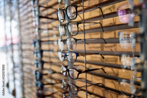 Different eyeglasses frames on a wall in modern optical store. Retail store background.