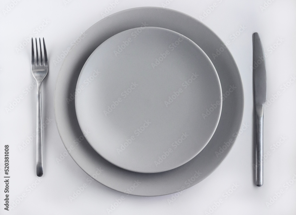 Grey empty plates with silver cutlery on the white table decorated by dried flowers Grey empty plates with silver cutlery on the white table decorated by dried flowers