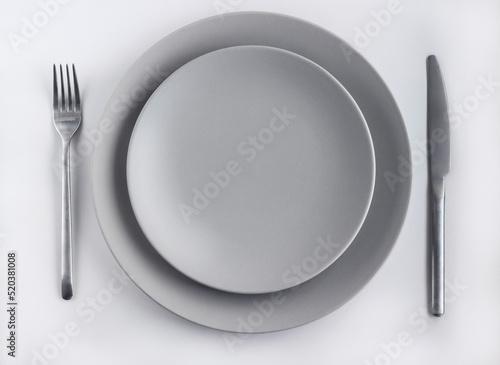 Grey empty plates with silver cutlery on the white table decorated by dried flowers