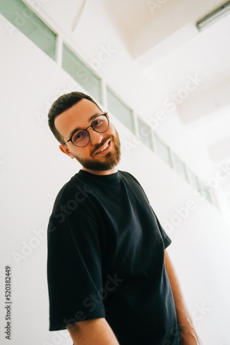 Portrait of stylish caucasian man in eyeglasses and black t shirt in bright living room.