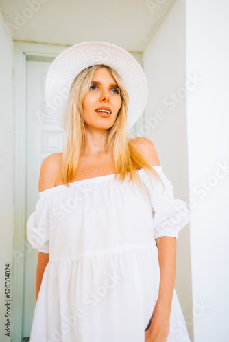 Portrait of attractive caucasian woman with blonde hair in white dress and hat, posing .