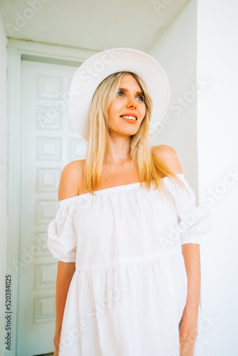 Portrait of attractive caucasian woman with blonde hair in white dress and hat, posing .