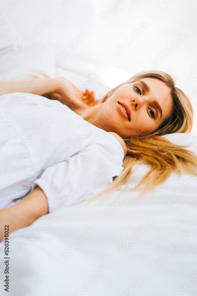 Portrait of attractive caucasian happy woman with blonde hair, lying on a bed with white blanket on sunny day. Portrait of attractive caucasian happy woman with blonde hair, lying on a bed with white blanket on sunny day.