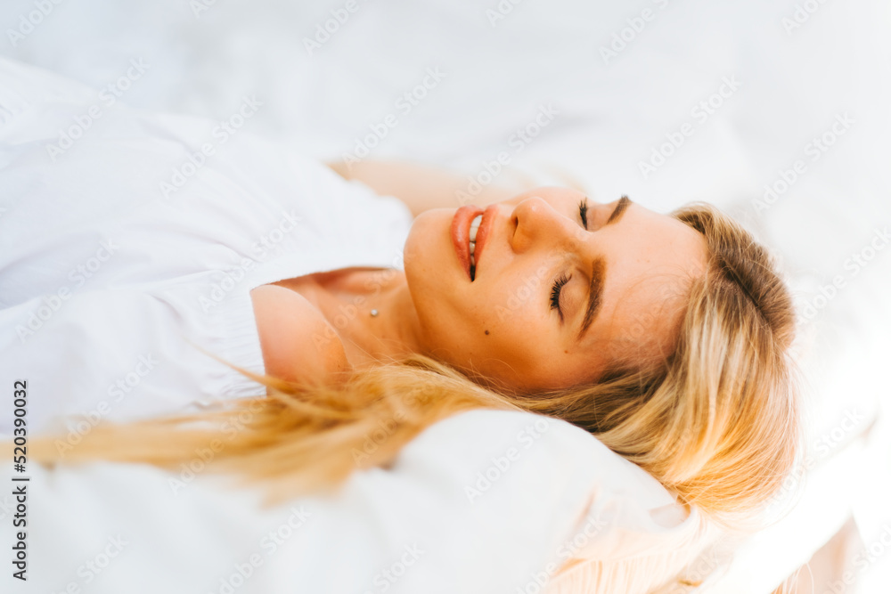 Portrait of attractive caucasian happy woman with blonde hair, lying on a bed with white blanket on sunny day. Portrait of attractive caucasian happy woman with blonde hair, lying on a bed with white blanket on sunny day.