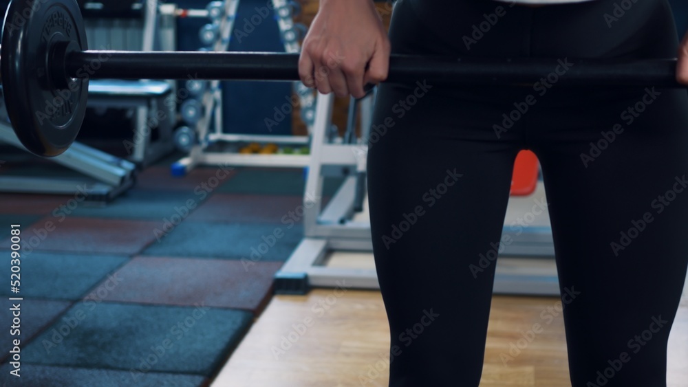Athletic woman pumps muscles using a barbell with a weight. Classes in the gym using extreme bar weights. Reducing excess weight in the gym due to physical activity. Physical exercise.