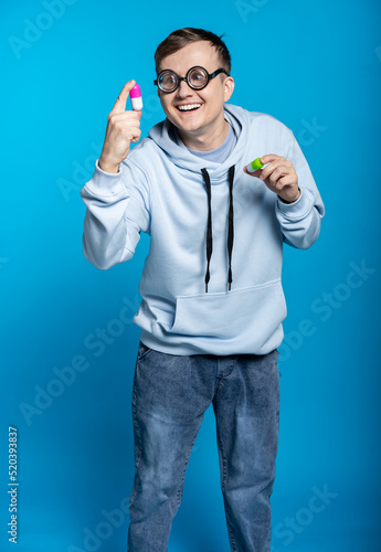 a funny guy in a blue sweatshirt and jeans and round glasses is holding big pills. blue background. funny batan, smart guy