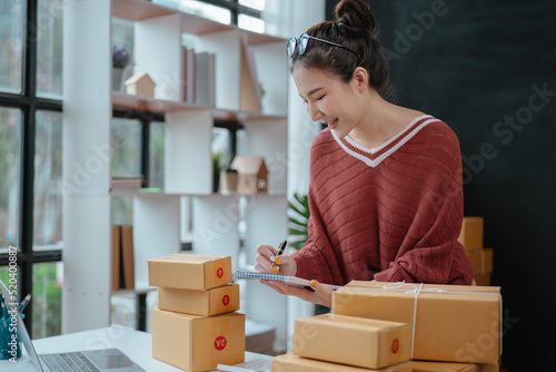 Business woman happy and cheerful for successful for receiving orders from customer via laptop with a lot of parcel boxes for shipping. © aksonsat