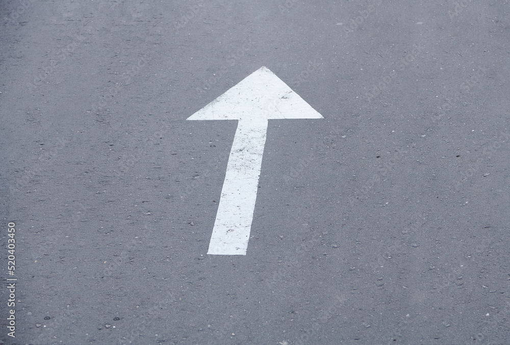 White arrow sign on the street. Directional arrow painted on pavement asphalt. Direction for traffic safety way. Symbol of crossroads. Pointer on gray asphalt floor.