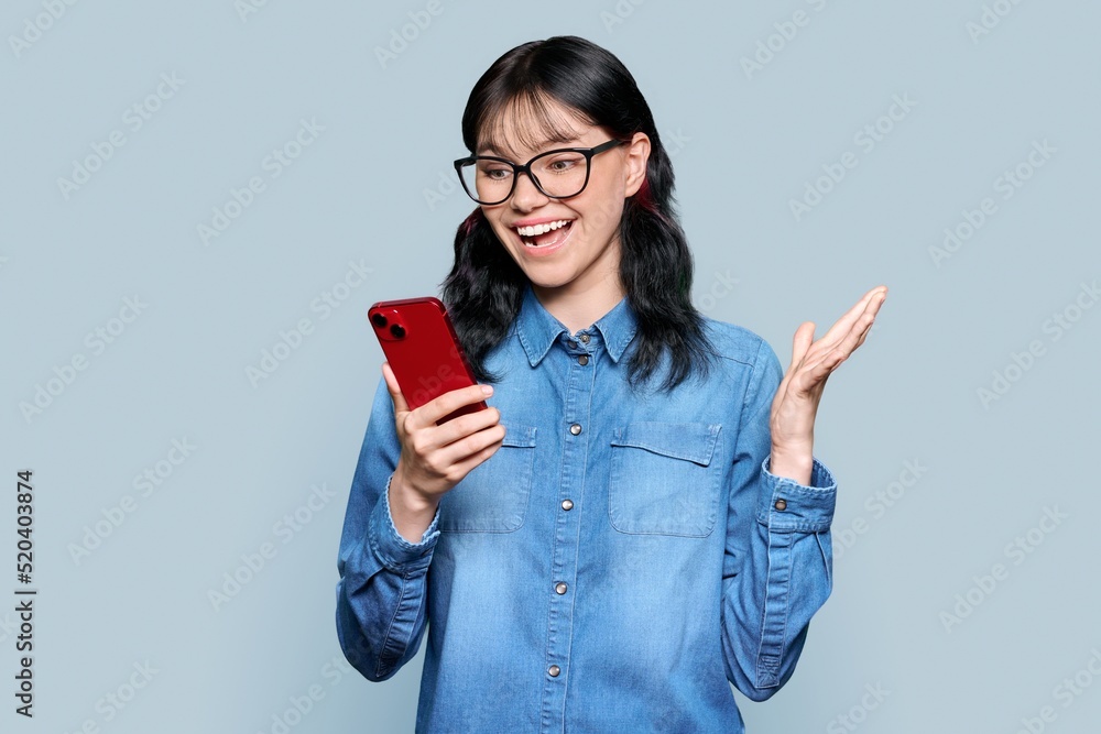 Surprised teenage girl looking at smartphone screen on gray background