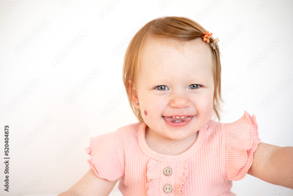 Portrait of a charming funny red-haired baby girl with blue eyes and a birthmark on her cheek. Hemangioma. Light background. Lifestyle Portrait of a charming funny red-haired baby girl with blue eyes and a birthmark on her cheek. Hemangioma. Light background. Lifestyle