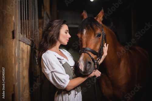 Young beautiful girl with the horse in the stable.