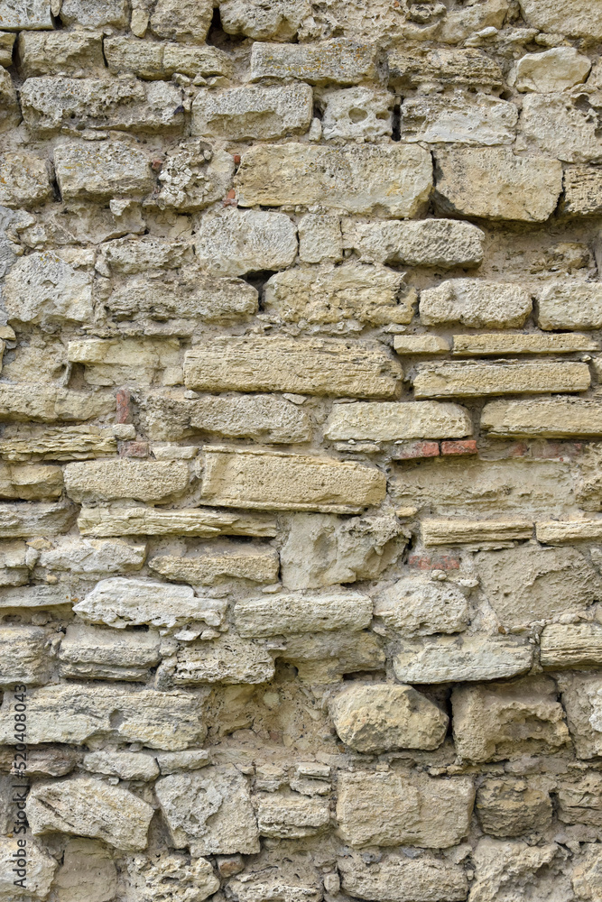 Masonry wall of old stone blocks of limestone. Background texture of ancient brick wall. Full frame. Vertical photo. Selective focus. Masonry wall of old stone blocks of limestone. Background texture of ancient brick wall. Full frame. Vertical photo. Selective focus.