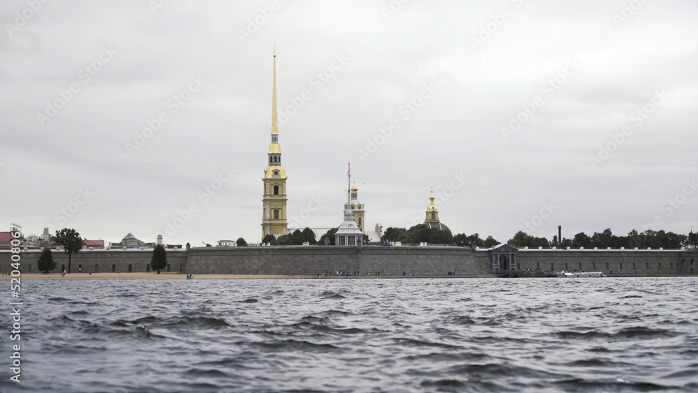 Close up of small waves of neva river and the golden spire of the Peter and Paul fortress. Action. Cloudy sky above the Petropavlovskaya fortress and Neva river.