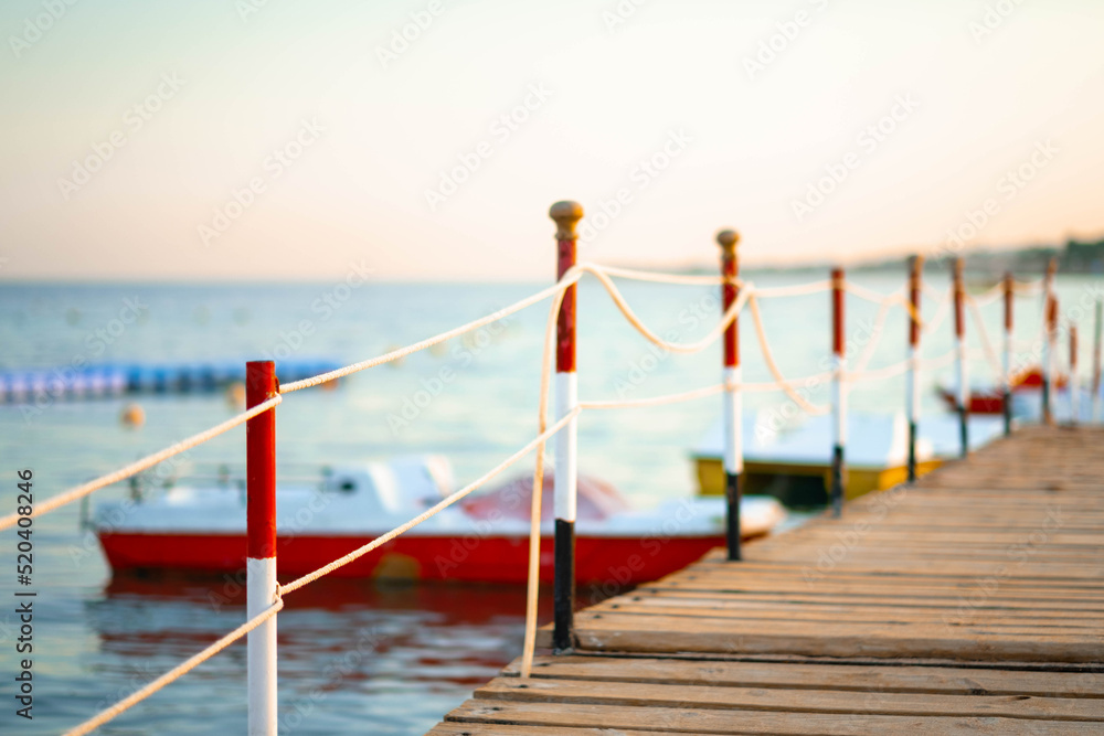 Naklejka premium Atmospheric wooden jetty on over the beautiful beach with blue sky, wooden pier with small boats at summer sunset