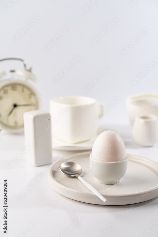 White egg with white plates, cup and alarm clock over white background for breakfast White egg with white plates, cup and alarm clock over white background for breakfast