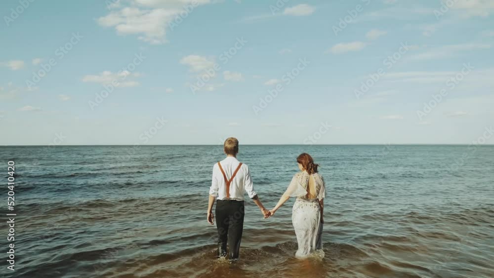 Happy couple together walking through the beach side they feeling great and very romantic, holding hands and with feet walking on water. Happy couple together walking through the beach side they feeling great and very romantic, holding hands and with feet walking on water.
