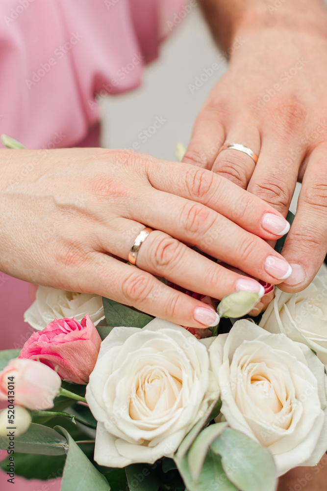 the hands of the bride and groom with rings over a bouquet of flowers the hands of the bride and groom with rings over a bouquet of flowers