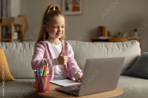 Smiling School Kid Girl Gesturing Like To Laptop At Home