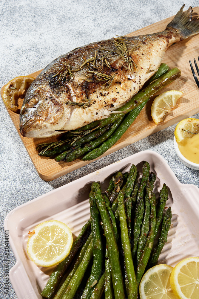dorado fried on a wooden board next to asparagus sauce and a black fork with a knife dorado fried on a wooden board next to asparagus sauce and a black fork with a knife