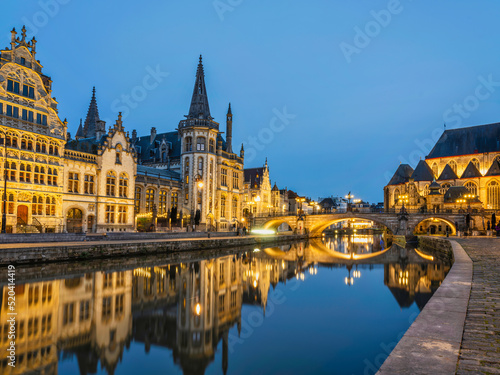 Historic medieval building illuminated at dusk on Leie river in Ghent, Belgium