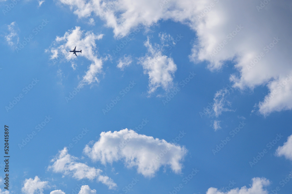 The passenger airplane is flying far away in the blue sky and white clouds. Aircraft in the air. Light background or backdrop about international passenger air transportation The passenger airplane is flying far away in the blue sky and white clouds. Aircraft in the air. Light background or backdrop about international passenger air transportation