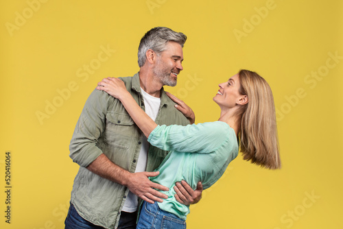 Loving middle aged woman and her husband dancing and having fun on yellow studio background