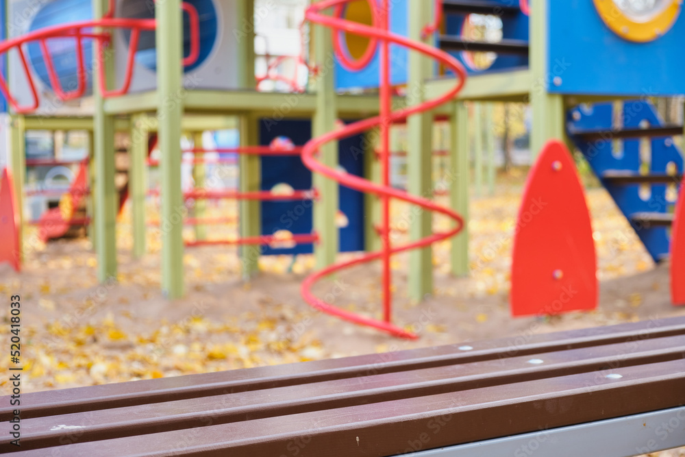 Empty playground in autumn, yellow leaves and play complex in blur and close up plank bench