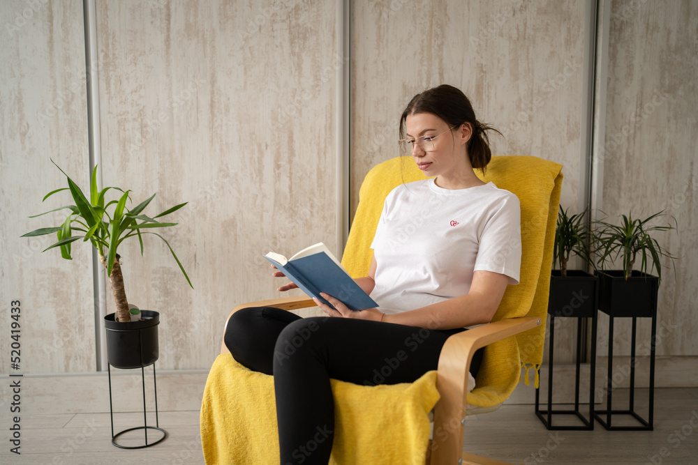 one woman young adult female read book while sitting in chair at home