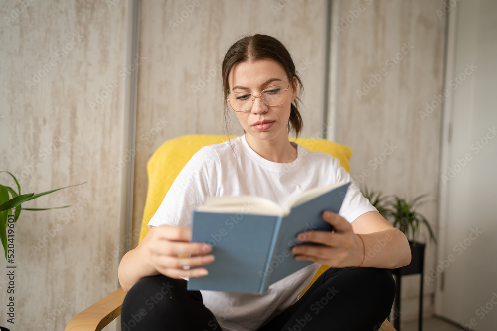 one woman young adult female read book while sitting in chair at home one woman young adult female read book while sitting in chair at home