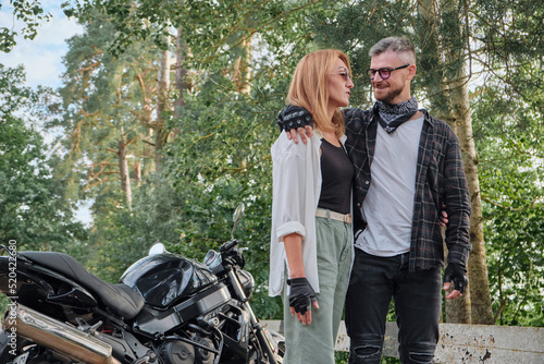 Middle age couple hugging and having fun on a motorcycle, traveling together on a forest road