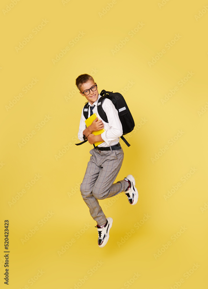School break. Cheerful mischievous schoolboy in uniform with a backpack jumps on a yellow background. Beginning of holidays. Back to school.