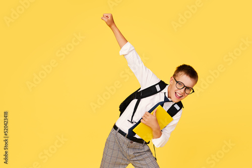 School break. Cheerful mischievous schoolboy in uniform with a backpack jumps on a yellow background. Beginning of holidays. Back to school.